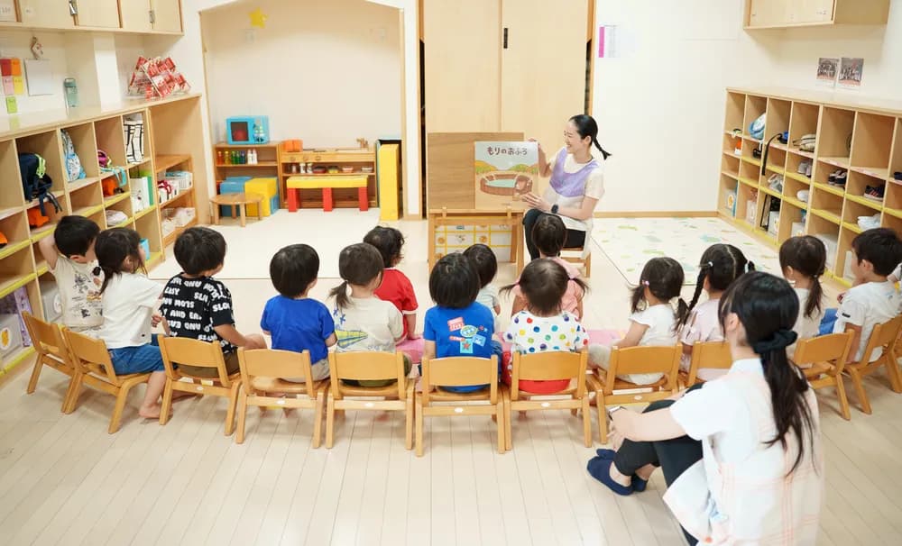 ビッグブックを読み聞かせる保育士と、聞き入る園児たちの様子