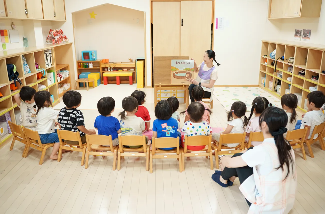 大型絵本を読み聞かせる保育士と、輪になって座る園児たち