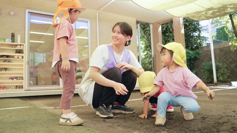 園庭でしゃがみ、園児と同じ目線で向き合う保育士